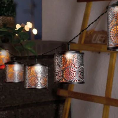 A string of solar-powered lanterns hanging outdoors, with a ladder and greenery in the background.