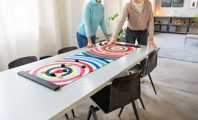 Two people playing a colorful curling game on a table in a room.