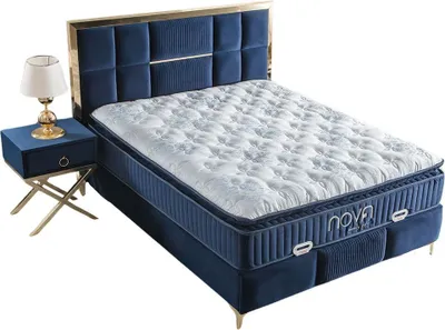 A blue upholstered bed with a mattress and a nightstand with a lamp.