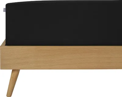 A close-up side view of a black fitted sheet on a wooden bed frame.