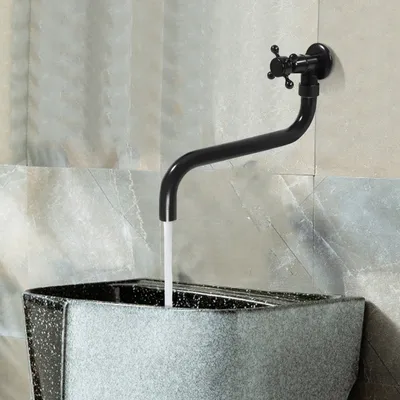 A black faucet with water running into a speckled gray basin against a tiled wall.