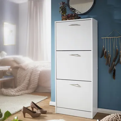 A white shoe cabinet with three drawers is shown in a bedroom setting, with shoes placed on the floor in front of it.