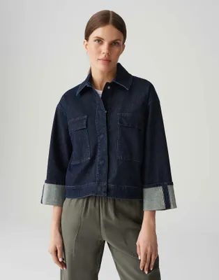 A woman wearing a denim jacket and green pants against a white background.