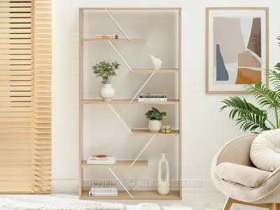 A modern, narrow bookshelf with a unique diagonal support design, styled with books, vases, and plants in a bright, airy room. A comfortable armchair and a framed abstract artwork are visible in the background.