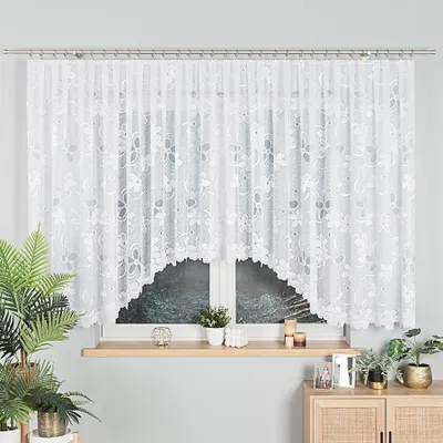 A white lace curtain with a floral pattern hangs over a window. Decorative items are placed on the windowsill and a cabinet.