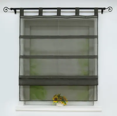A sheer gray Roman blind is hung on a window, with a small pot of sunflowers on the windowsill below.