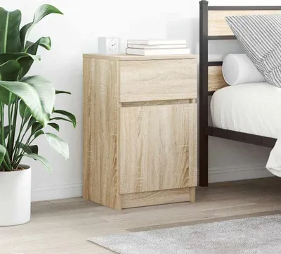 A wooden nightstand is placed next to a bed, with a plant in a pot on the left.