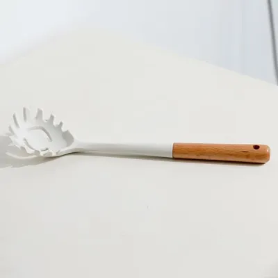 A white spaghetti spoon with a wooden handle lies on a white surface.