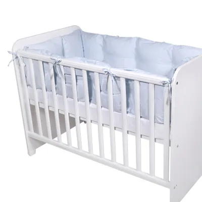 A white baby crib with a light blue bumper pad inside.