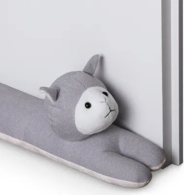 A stuffed animal shaped like a cat is leaning against a white wall.