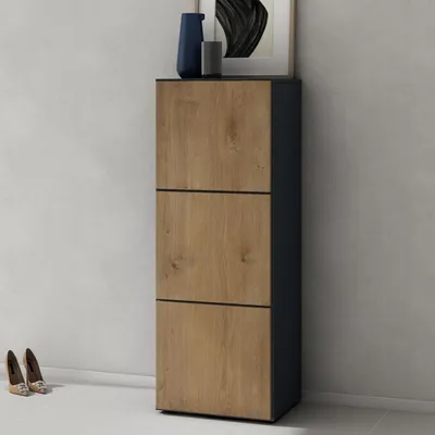 A shoe cabinet with three drawers is shown in a room with a light gray wall and white floor. Two pairs of shoes are placed on the floor in front of the cabinet.