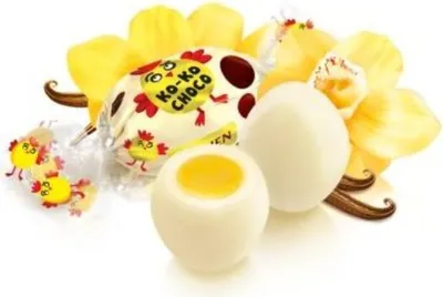 A close-up of white chocolate candies shaped like eggs, with yellow filling, surrounded by yellow orchid petals and vanilla beans.