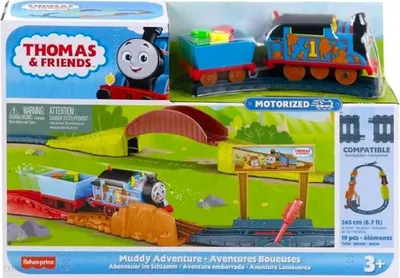 The image shows the packaging of a Thomas & Friends "Muddy Adventure" motorized train set. The packaging displays the product in action on a track with a bridge and a billboard.