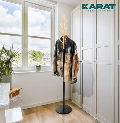 A room with a window, a plant, a table, a chair, a wardrobe, and a coat rack with a jacket on it.