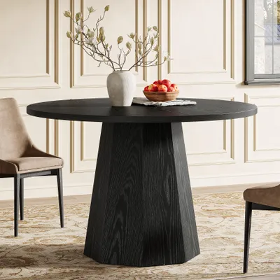 A round black dining table with a unique pedestal base, set in a dining room with a chair and decorative items on the table.