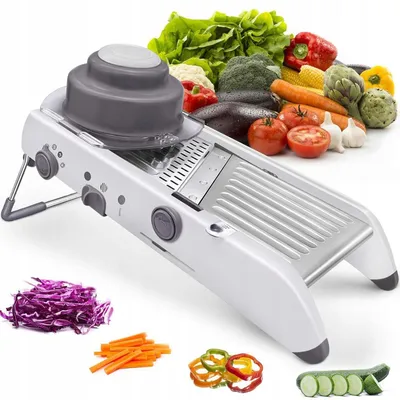 A white mandoline slicer is displayed prominently in the foreground, with a variety of fresh vegetables arranged in the background and around the slicer. Sliced vegetables are also shown in the foreground.
