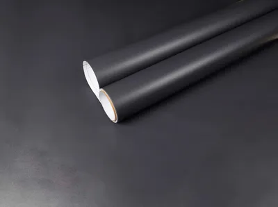 Two rolls of matte black paper or vinyl are arranged diagonally on a dark gray surface.