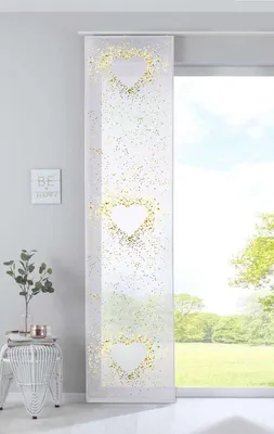A white panel curtain with gold heart patterns hanging in front of a window with a view of greenery.