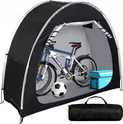 A bicycle stored inside a black tent-like structure, with a soccer ball and a blue storage box nearby. A rolled-up black bag is shown in the foreground.