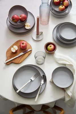 A table setting with plates, bowls, cutlery, apples, a candle, and a vase.