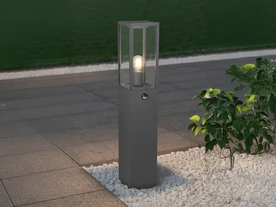 A modern outdoor lamp post is situated on a paved walkway with white gravel and greenery.