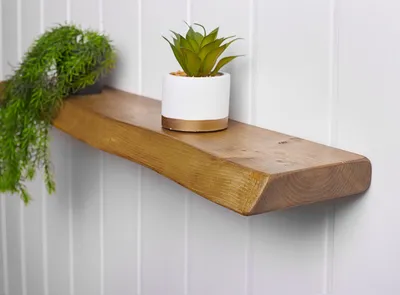 A wooden shelf with two decorative plants on it, mounted on a wall with vertical paneling.