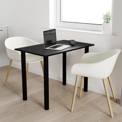 A black table with black legs is set up with a laptop and a mug, next to two white chairs, in a room with a window.