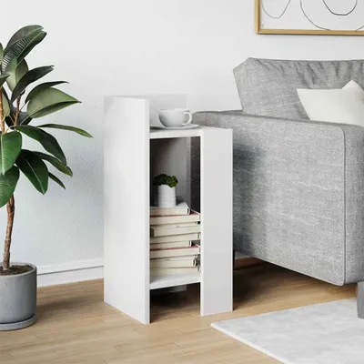 A white side table with books and a plant next to a gray sofa.
