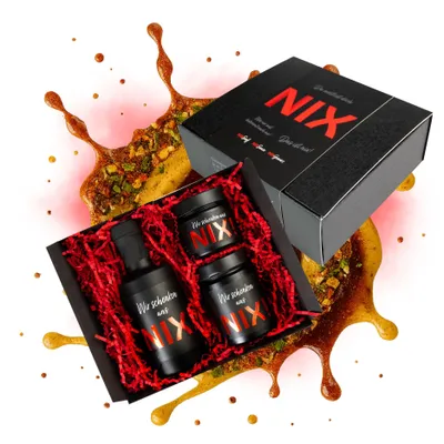 A gift set of mustard products, including a bottle and two jars, arranged in a black box with red crinkle paper. The set is surrounded by splashes of sauce and spices.