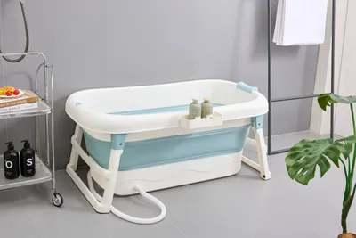 A foldable bathtub is set up in a bathroom setting, with a shelf holding bottles and a plant nearby.