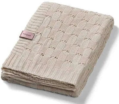 A folded beige knitted baby blanket with a pink brand tag.
