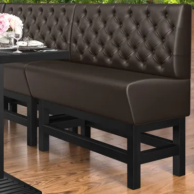 A dark brown tufted leather bench seat with a black metal frame, placed outdoors on a wooden deck with greenery in the background.