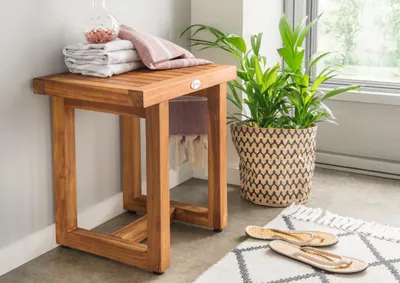 A wooden side table with towels and a plant in a basket next to it.