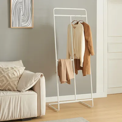 A coat rack with clothes and pants is placed next to a sofa in a room.