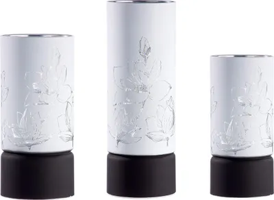 Three white cylindrical LED candle holders with embossed silver floral designs and black bases, arranged side-by-side against a white background.