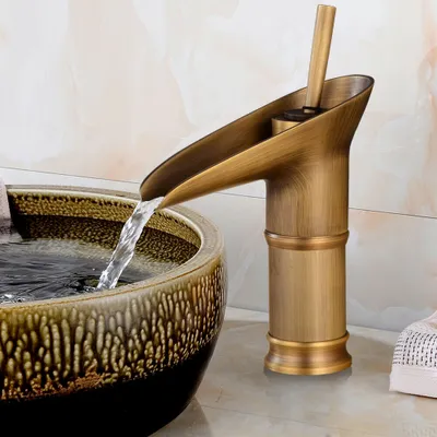 A close-up shot of a retro-style bronze faucet with water flowing into a decorative ceramic sink.