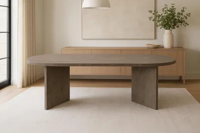 A modern oval dining table with a gray wood-look finish is shown in a well-lit dining room with a sideboard and artwork in the background.