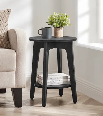 A black round side table with a plant and a mug on top, placed next to a beige sofa.