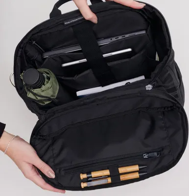 An open black backpack with various items inside, including a laptop, tablet, and a small umbrella.