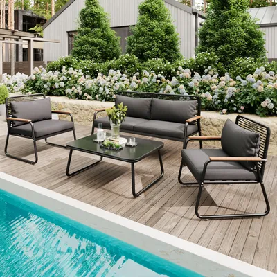 A patio furniture set is arranged on a wooden deck next to a swimming pool, with a lush garden and house in the background.