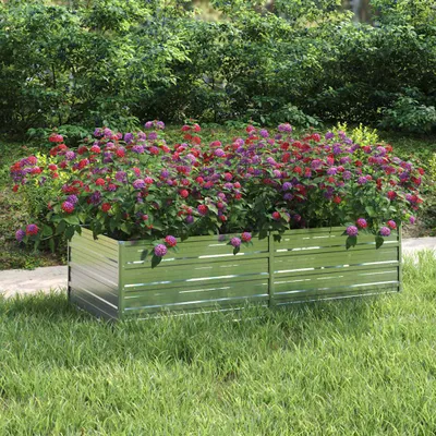 A metal raised garden bed filled with colorful flowers, set in a grassy yard with a backdrop of green bushes.
