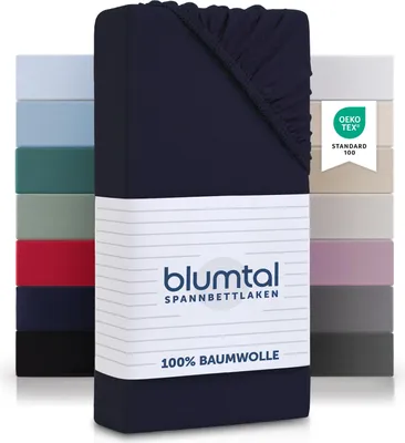 A stack of folded fitted sheets in various colors, with a dark blue fitted sheet prominently displayed in the foreground with packaging.