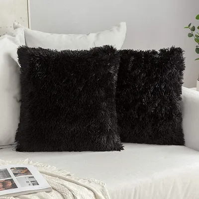 Two black fluffy throw pillows are placed on a white sofa.