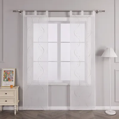 A sheer curtain with a wavy beaded pattern hangs in front of a window, with a small table and lamp visible to the side.