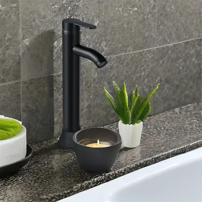 A black matte faucet is shown on a countertop next to a lit candle and a small potted plant.