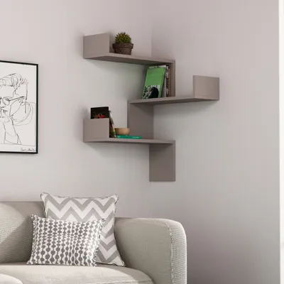 A corner shelf unit with books and a plant is mounted on a wall above a sofa with decorative pillows.