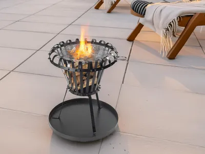 A fire pit with burning wood on a patio next to a lounge chair.