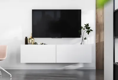 A modern white TV stand with a large black TV mounted above it, decorated with a few items.