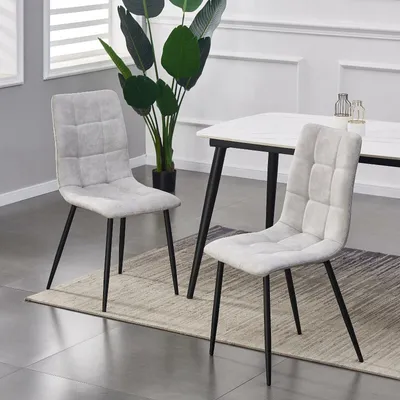 Two dining chairs are shown in a room setting, with a table and plant in the background.