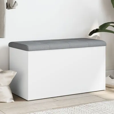 A white storage bench with a gray upholstered top is shown in a room setting.